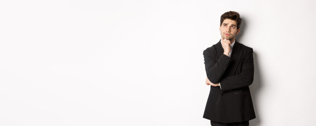 Portrait of handsome and stylish man in suit, thinking and looking at upper left corner, imaging something about christmas holidays, standing over white background - Dr.成井の毛髪LAB – AGA対策から植毛最新技術まで